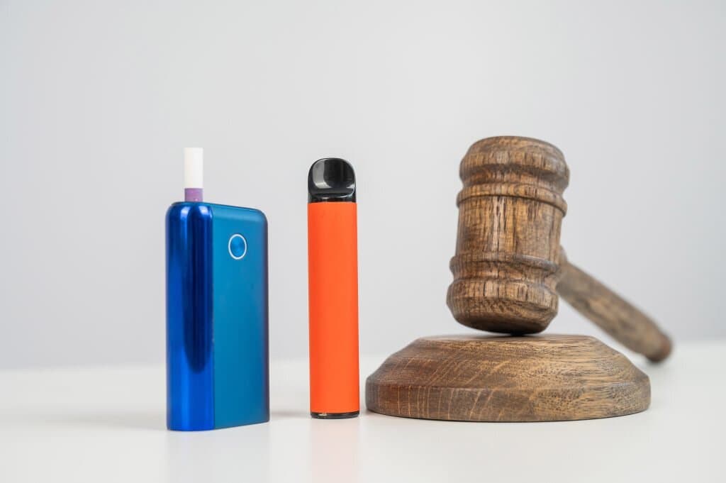 Vape device and e-cigarette standing next to a wooden gavel, symbolizing vaping regulations and legal considerations in the vaping community.
