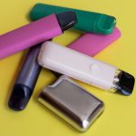 Assorted disposable vape pens and devices on a yellow background.