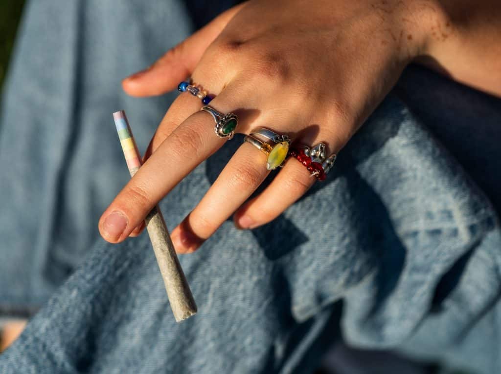 A hand with multiple rings holding a infused pre-roll joint,