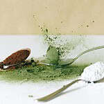 Close-up of green and white vape flavor powders being scooped with metal spoons, highlighting ingredients used in e-liquid flavoring.