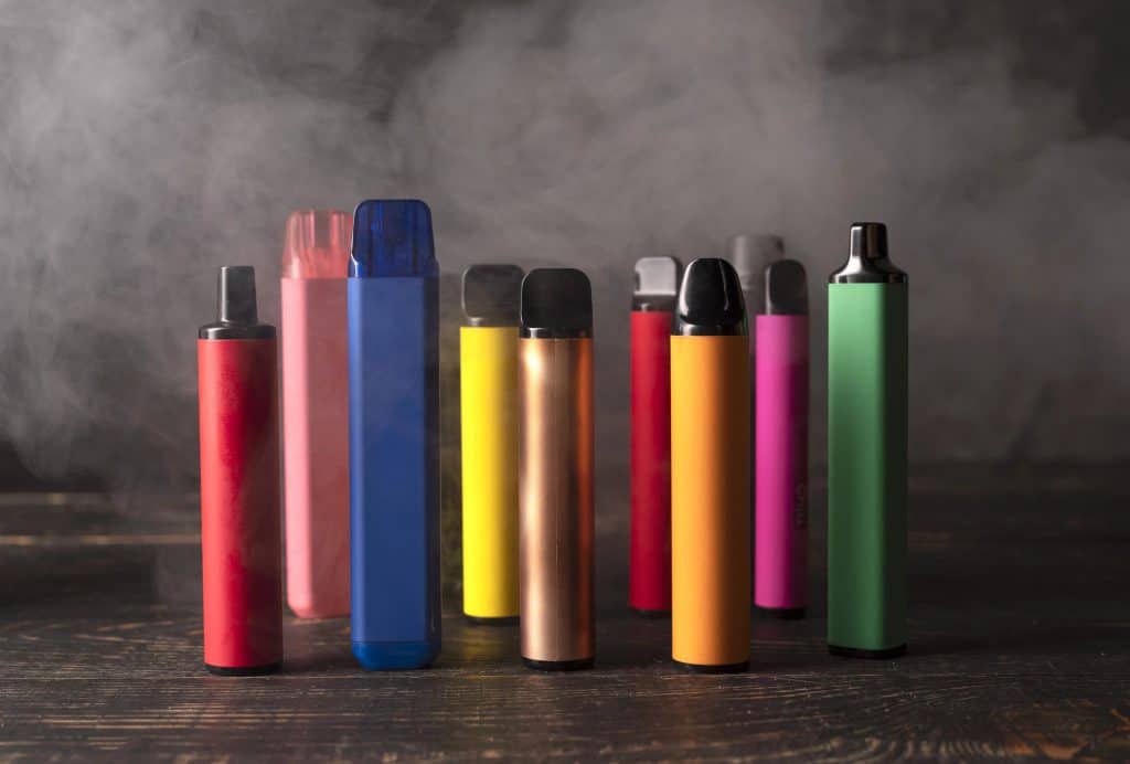 Assorted colorful vape devices and e-liquid bottles arranged on a dark wooden surface, showcasing a variety of flavors and styles for vaping enthusiasts.