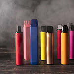 Assorted colorful vape devices and e-liquid bottles arranged on a dark wooden surface, showcasing a variety of flavors and styles for vaping enthusiasts.